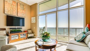 A spacious living room with a large window, a flat-screen TV, a round coffee table, and a sofa. - Luxe 28th-Floor S Tower Condo: Ocean & SpaceX View (South Padre Island)