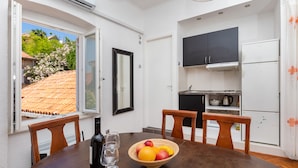 A dining area with a table, chairs, a bowl of fruit, a wine bottle, and a wine glass. - Apartment Entre Les Jardins (Dubrovnik)