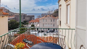A balcony with a table and chairs, overlooking a cityscape with buildings and a view of the sea. - Apartment Entre Les Jardins (Dubrovnik)