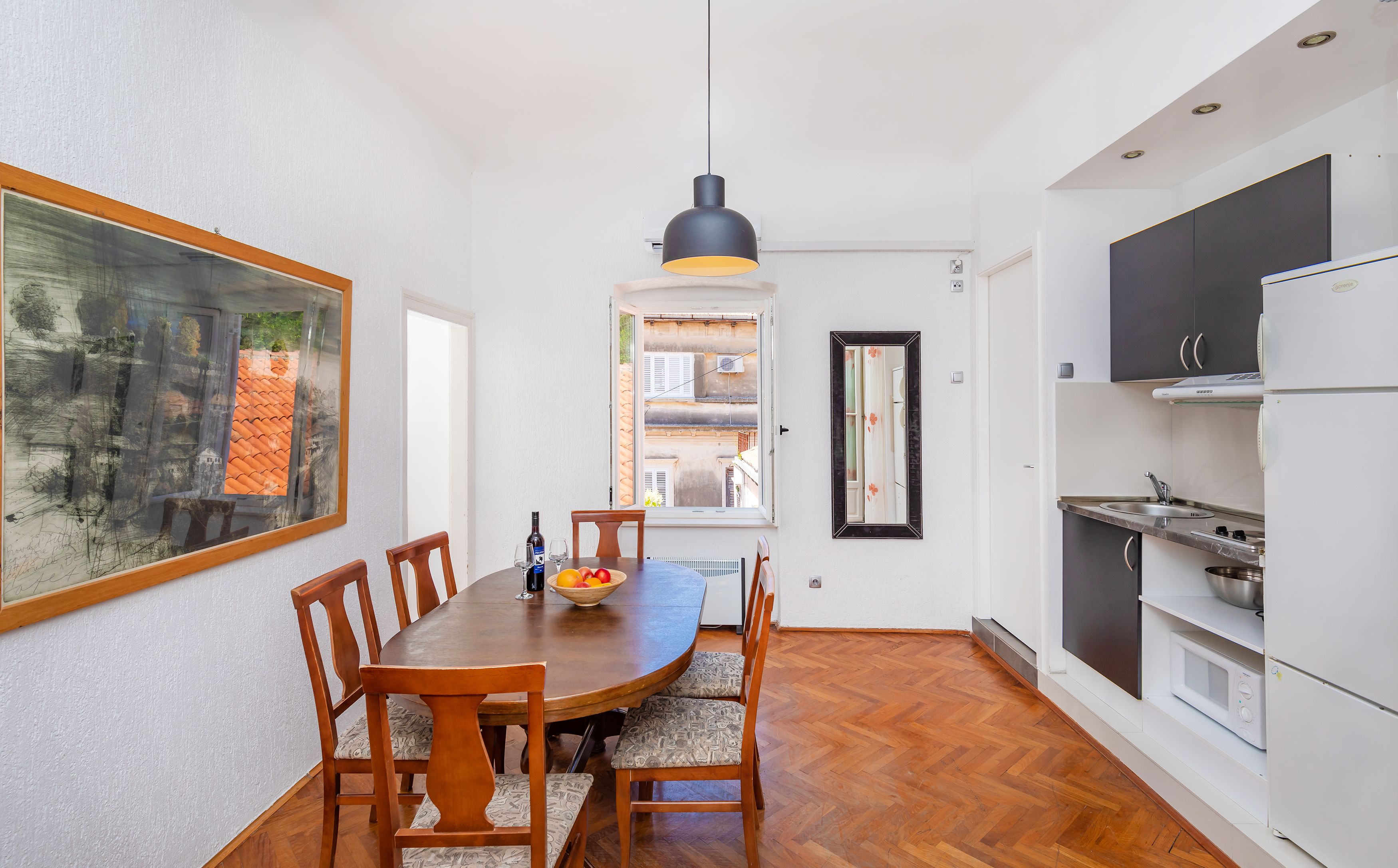A dining area with a wooden table and chairs, a hanging pendant light, and a view of a courtyard through a window.