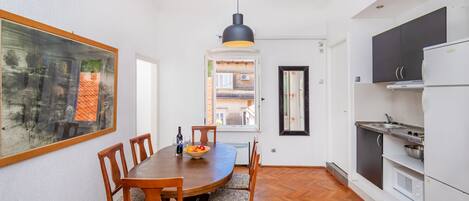 A dining area with a wooden table and chairs, a hanging pendant light, and a view of a courtyard through a window.