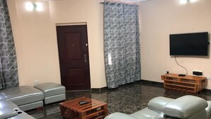 Una sala de estar con un sofá seccional, una mesa de centro de madera, un televisor de pantalla plana y una cortina estampada.
