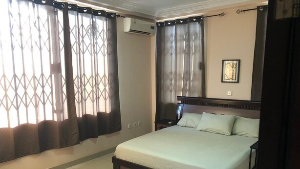 Un dormitorio con una cama grande, cortinas, un equipo de aire acondicionado y un cuadro en la pared.