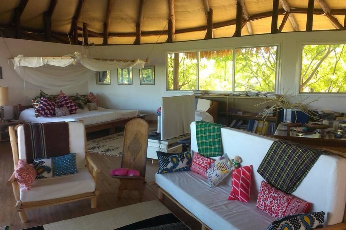 A cozy room with a bed, a sofa, a chair, and a desk. There are windows and a ceiling with wooden beams.
