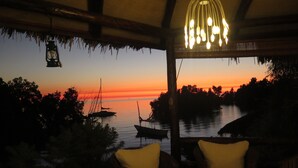 Une pièce offrant une vue sur le coucher de soleil sur l’eau, avec un luminaire suspendu et deux fauteuils.