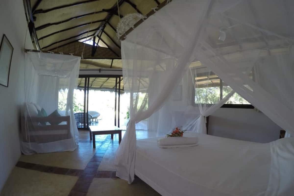 A room with a bed covered by a white canopy, a bench, and a table with a flower arrangement.