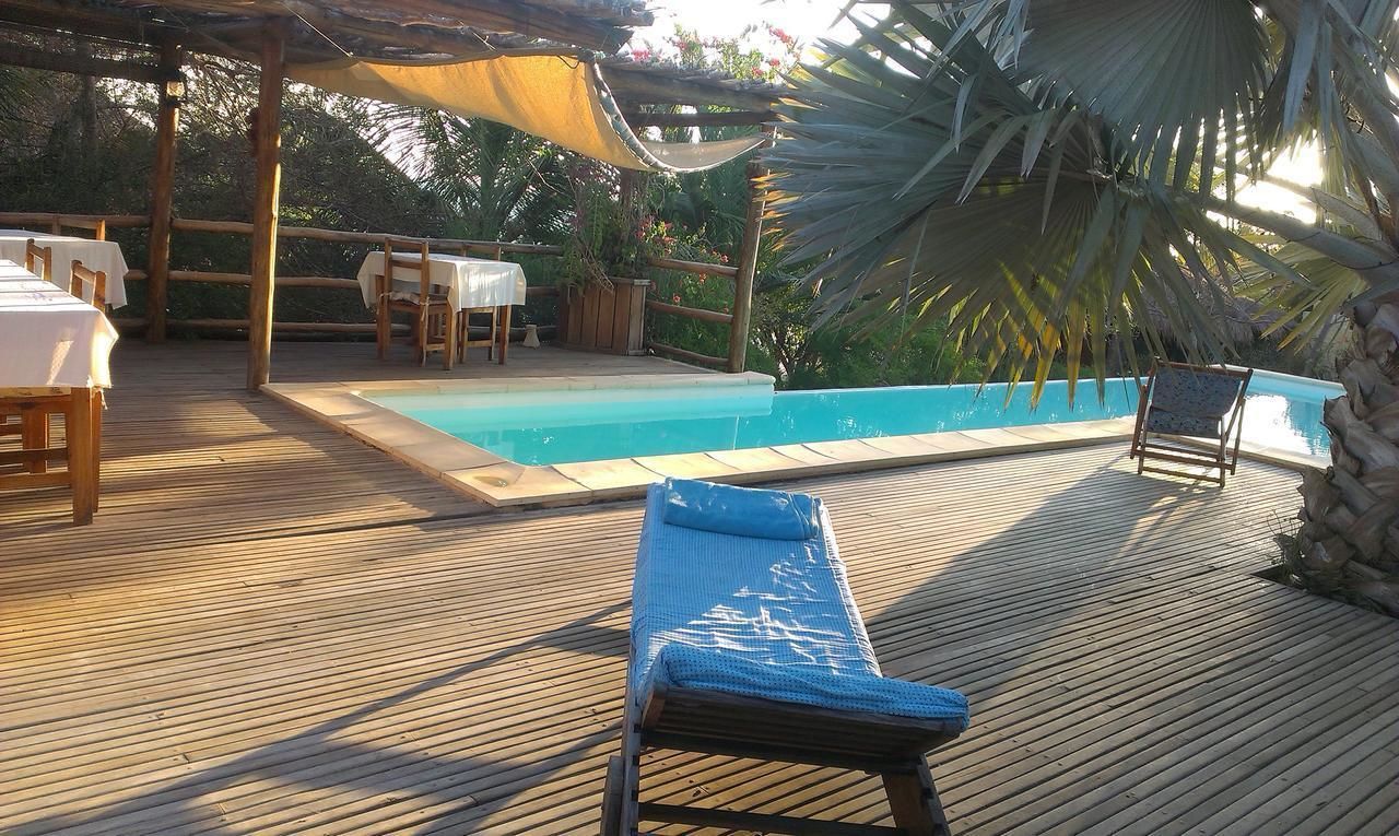 A wooden deck with a pool, lounge chairs, and tables with white tablecloths.