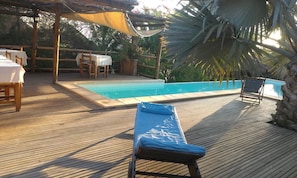 Una terraza de madera con piscina, sillas de descanso y mesas con manteles blancos.