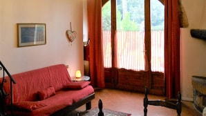 A cozy room with a red sofa, a small table with a lamp, a heart-shaped decoration, and a large window with curtains.