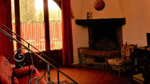 A cozy living room with a fireplace, a staircase, and a large window with curtains.