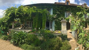Una casa con techo circular, paredes cubiertas de hiedra y un jardín con diversas plantas y flores.