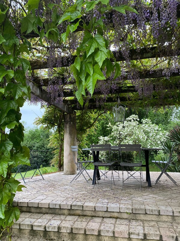 A garden with a pergola covered in purple flowers, a swing set, and a table and chairs.
