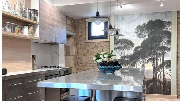 A modern kitchen with a large island, bar stools, and a stone accent wall.