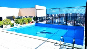 A rooftop pool with a city view, surrounded by potted plants and a safety fence. - Apartamento Jatiúca  Renovatio (Maceió)