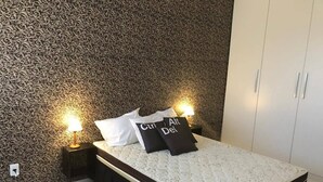 A bedroom with a patterned wallpaper, a white bed with black and white pillows, and bedside lamps. - Apartamento Jatiúca  Renovatio (Maceió)