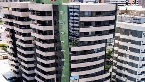 A high-rise building with multiple balconies and a green rooftop area. - Apartamento Jatiúca  Renovatio (Maceió)