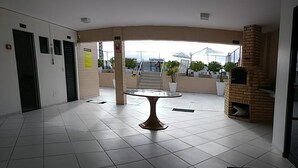 A spacious indoor area with a tiled floor, a central table, and a brick oven. - Apartamento Jatiúca  Renovatio (Maceió)