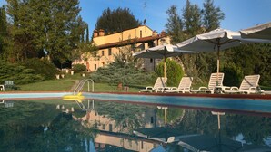 A swimming pool with lounge chairs and umbrellas, surrounded by greenery and a building in the background. - Lovely apartment for 6 people with pool, WIFI, TV and pets allowed, close to San Gimignano (Varna)