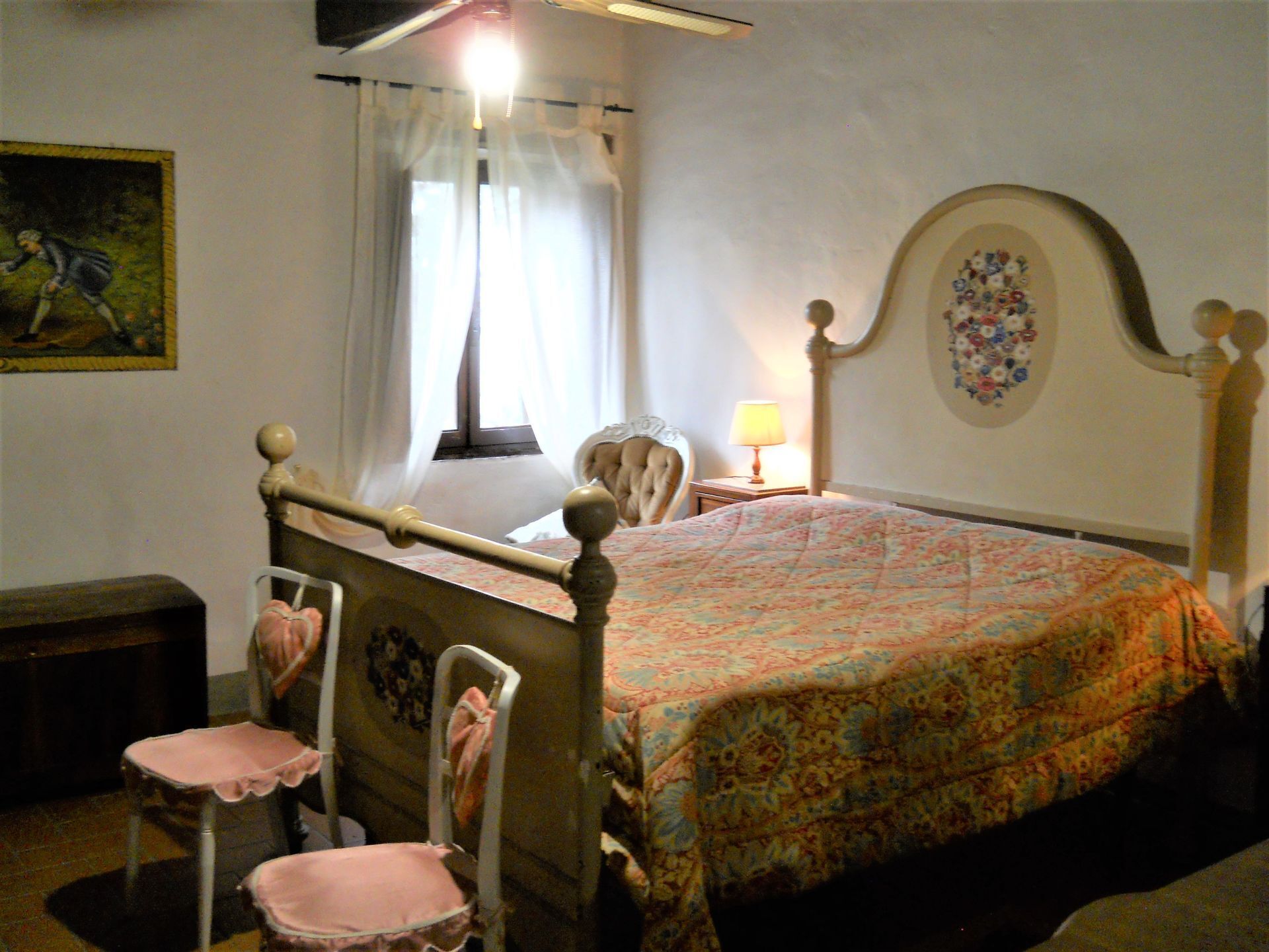 Une chambre à coucher avec un lit, une chaise, une table de chevet, une lampe et un tableau au mur.
