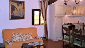 A cozy living room with a sofa, a small table, and a painting on the wall. There is a kitchen area with cabinets and a stove. - Lovely apartment for 6 people with pool, WIFI, TV and pets allowed, close to San Gimignano (Varna)