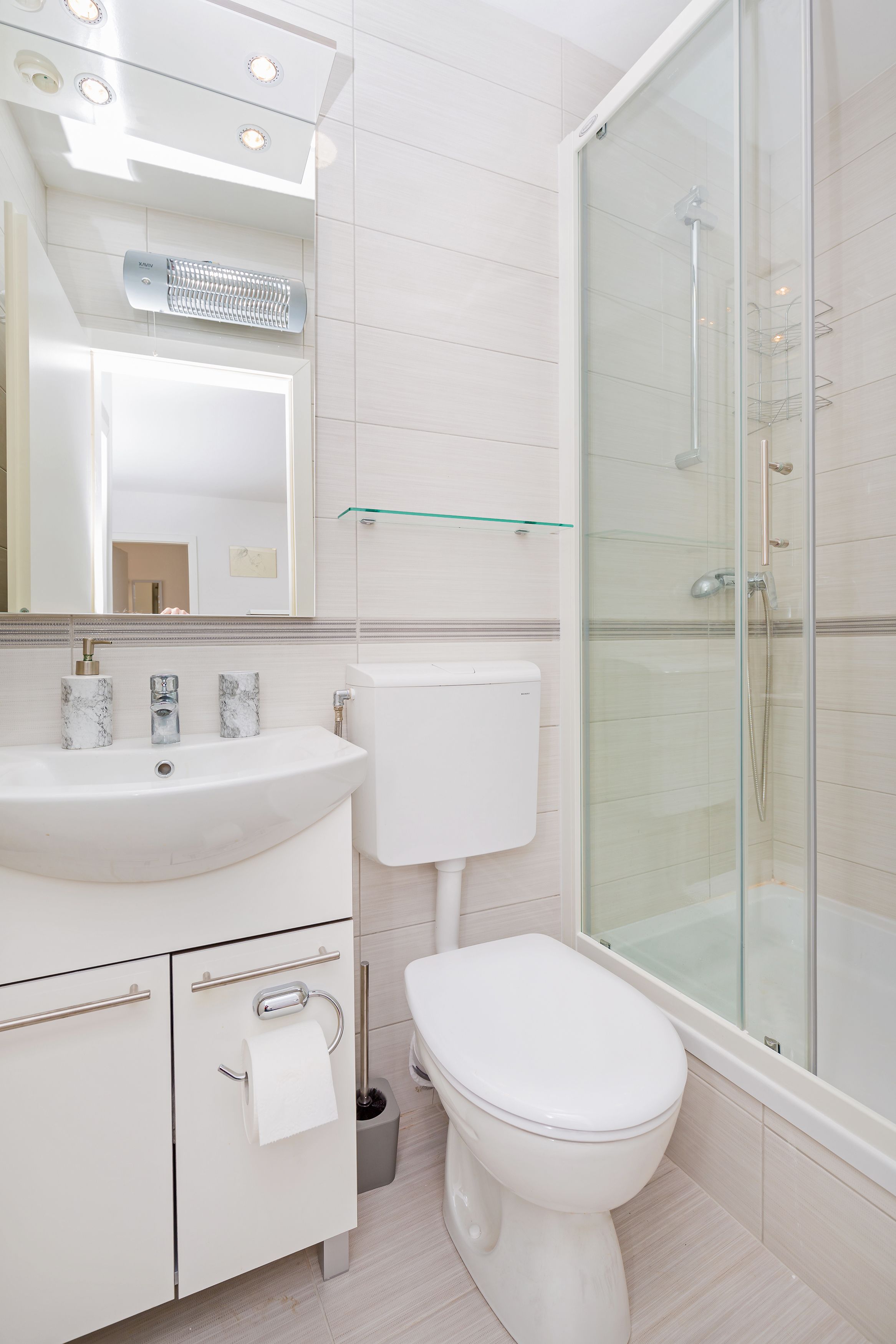 Een moderne badkamer met een wit wastafel, toilet en een douchecabine met glazen wanden.