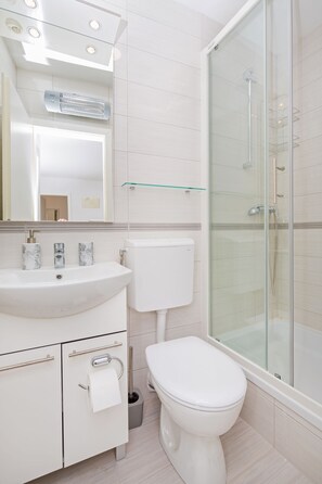 Une salle de bain moderne avec un lavabo blanc, des toilettes et une douche à parois de verre.