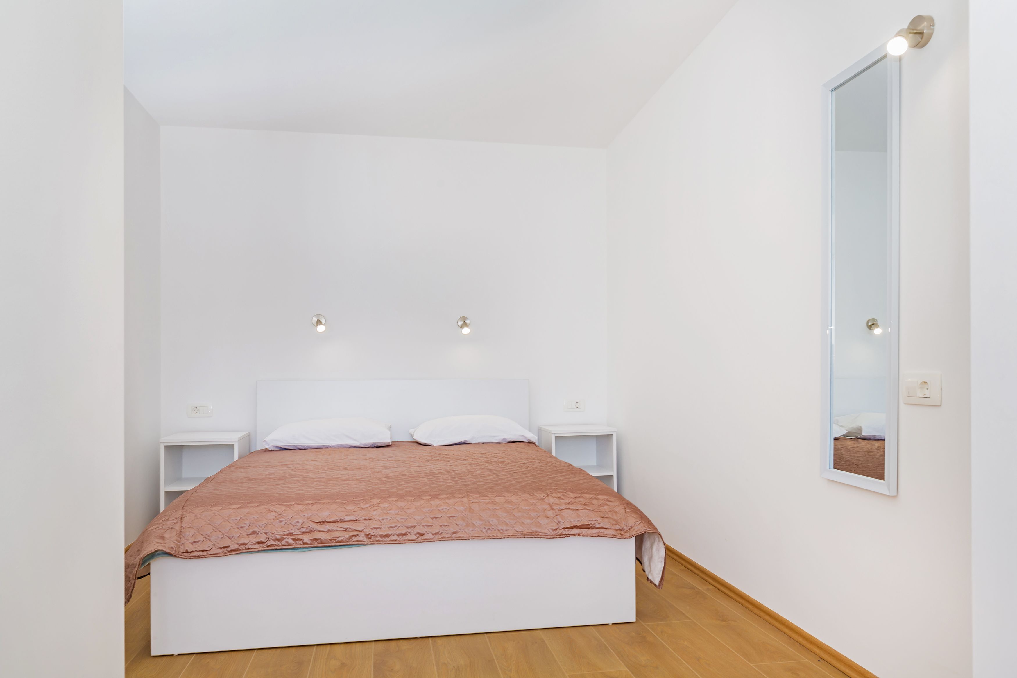 Une chambre à coucher comprenant un lit, deux tables de chevet, une commode, un miroir fixé au mur et un luminaire.
