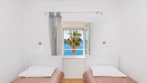 A bedroom with two beds, a window with a view of the sea, and a curtain. - Apartment View (Dubrovnik)