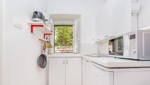 A compact kitchen with white cabinets, a microwave, and a window with a view of greenery. - Apartment View (Dubrovnik)