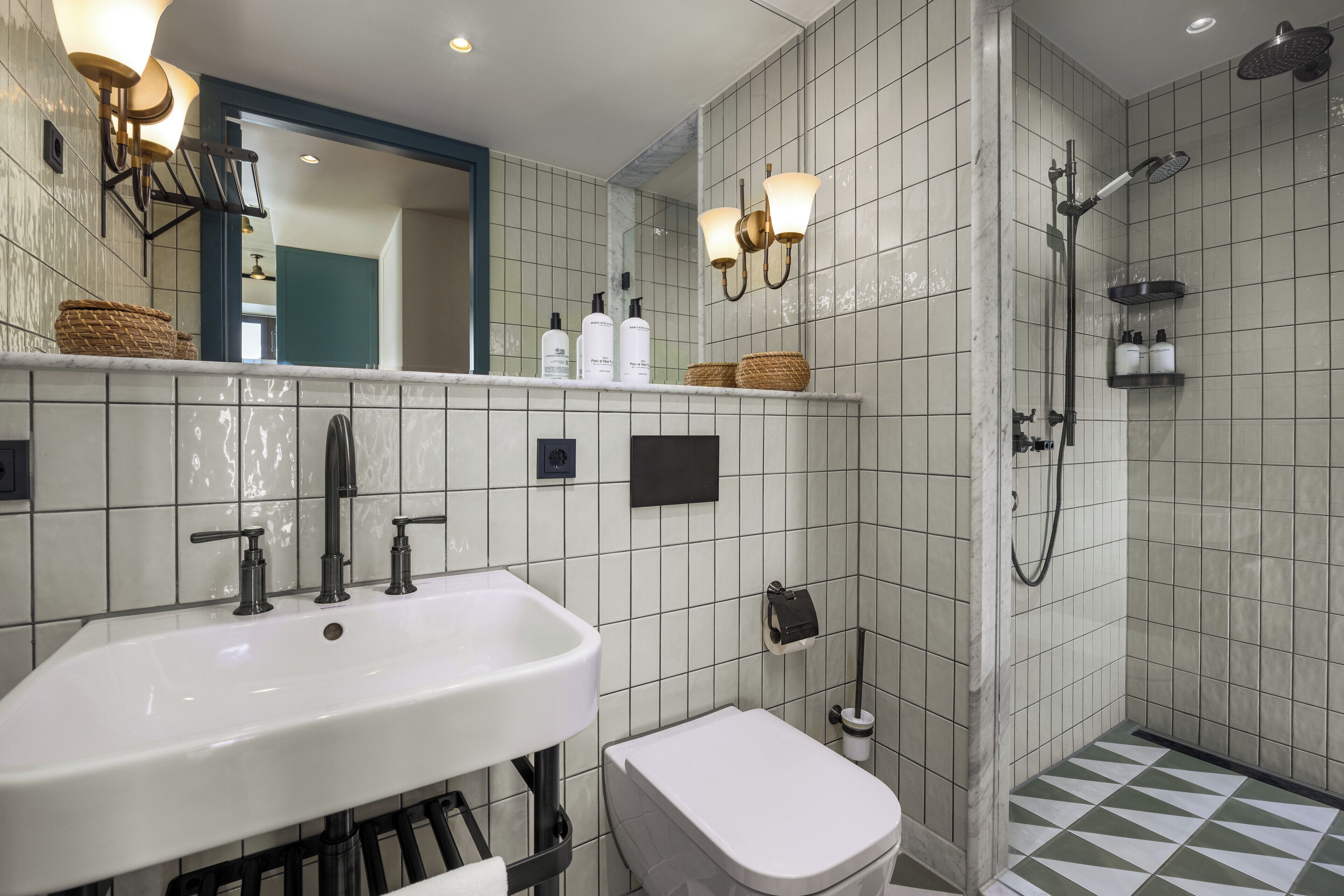 A bathroom with a white sink, a toilet, a shower with a handheld showerhead, and a mirror with wall sconces.