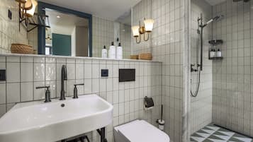 A bathroom with a white sink, a toilet, a shower with a handheld showerhead, and a mirror with wall sconces.