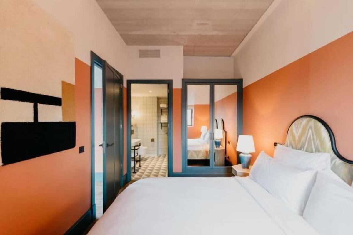 A hotel room with a bed, a wardrobe, a mirror, and a door leading to a bathroom.