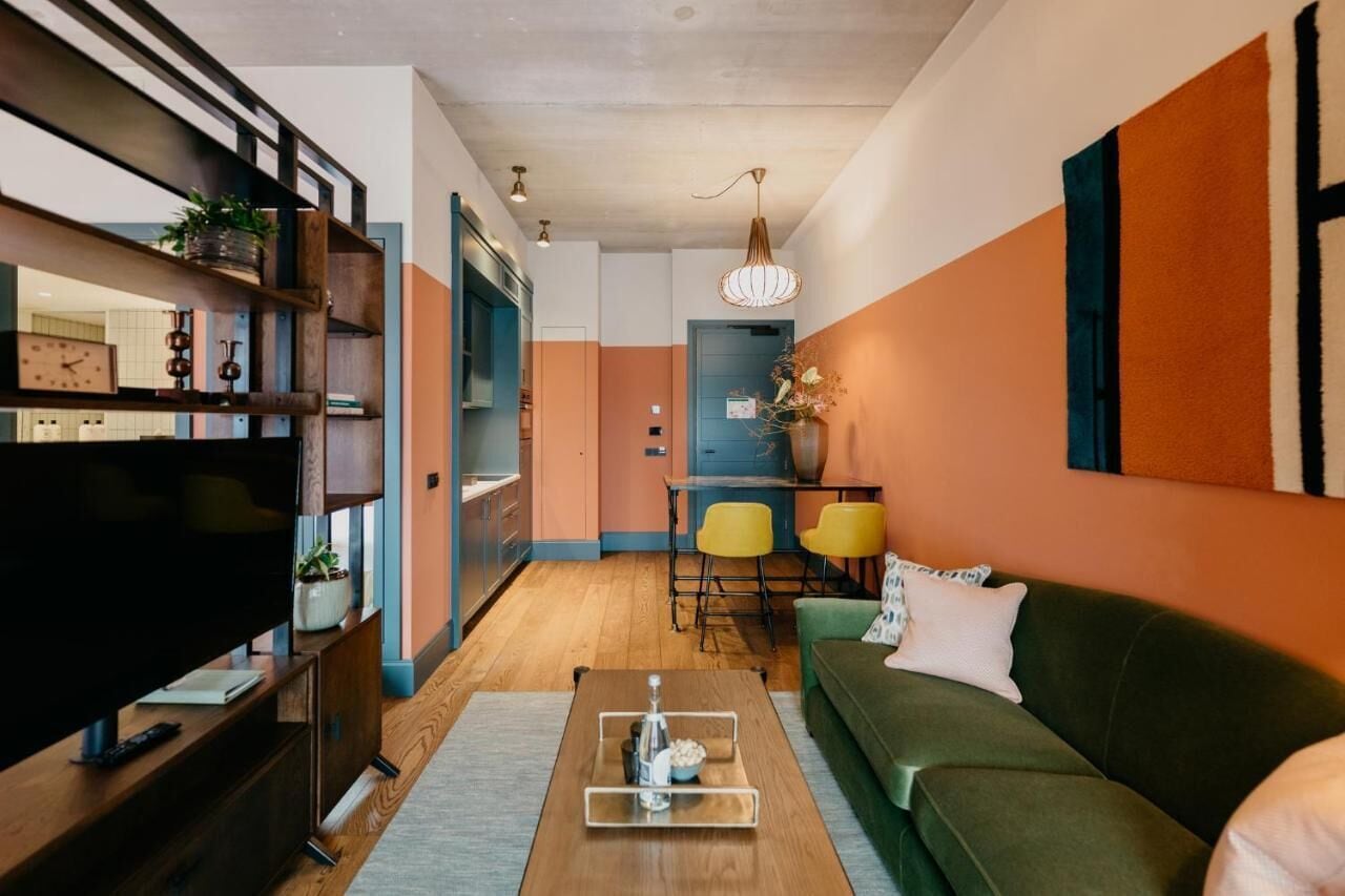 A modern living room with a TV, wooden coffee table, green sofa, and yellow chairs.