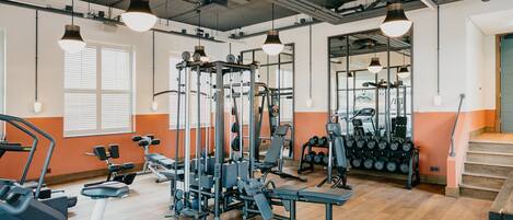 Ein Fitnessraum mit Trainingsgeräten, Holzböden und großen Fenstern.