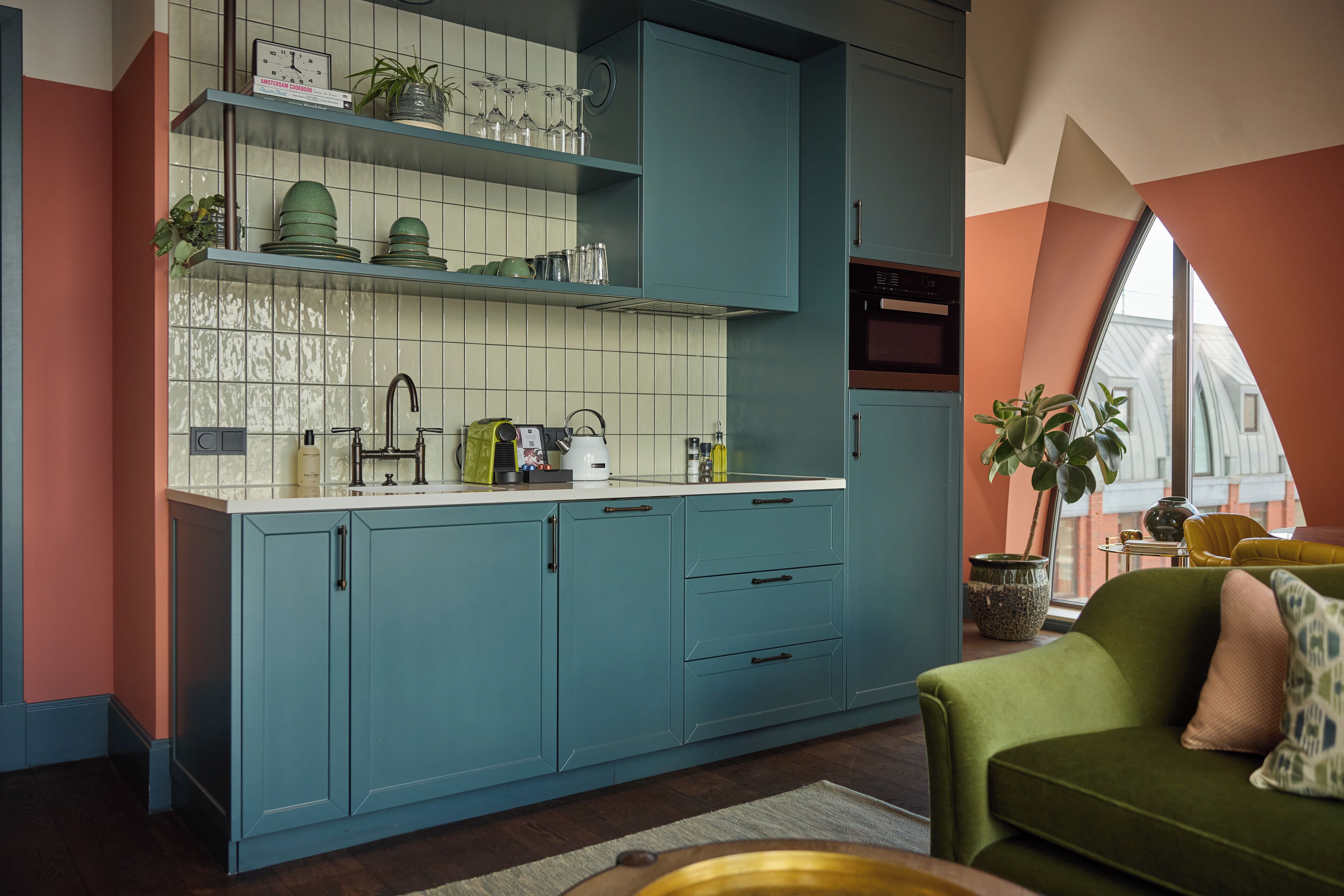 A modern kitchen with teal cabinetry, a tiled backsplash, and a window providing natural light.