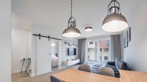 A modern living room with a wooden dining table, grey sofas, and a TV mounted on the wall. - Apartamenty Sun & Snow Angielska Grobla (Gdansk)