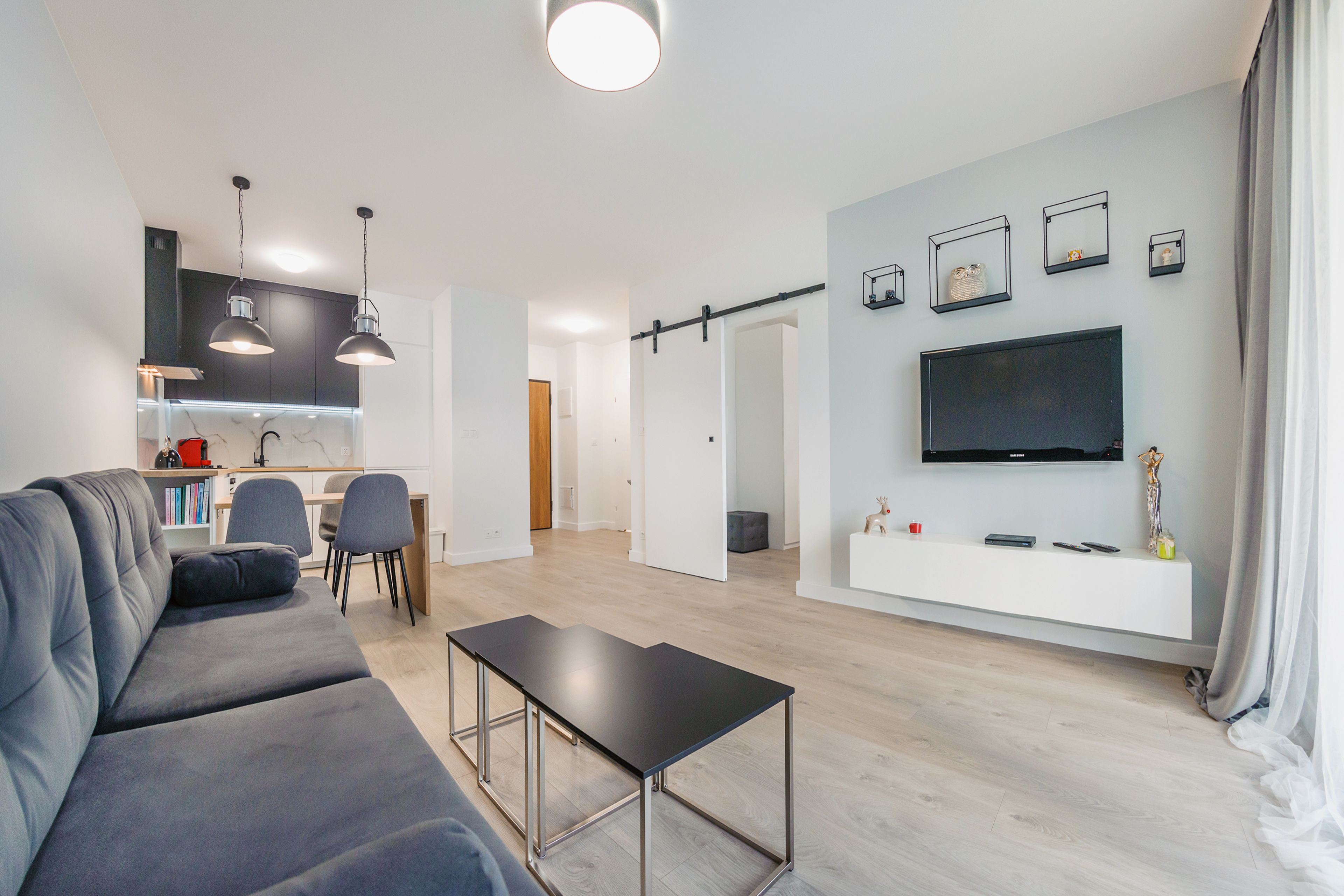 A modern living room with a grey sofa, a black coffee table, and a TV mounted on the wall.