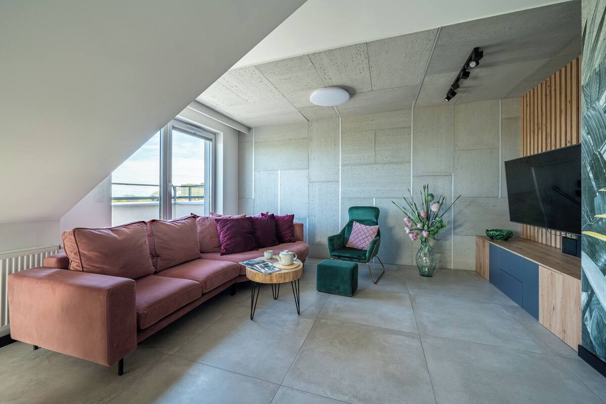A modern living room with a pink sofa, a green armchair, a small coffee table, and a flat-screen TV mounted on the wall.
