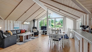 Un vaste espace de vie doté d’un plafond en bois, d’un ensemble de canapés, d’une table à manger avec des chaises, et d’un coin cuisine avec un comptoir et des ustensiles.