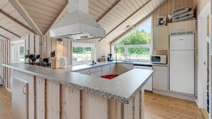 Une cuisine moderne dotée d’un îlot central, de poutres en bois, de grandes fenêtres et d’appareils électroménagers de base.