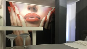 Ein modernes Hotelzimmer mit einem großen Bett, einem kleinen Tisch mit zwei Hocker und einem an der Wand befestigten Fernseher, der ein Bild von Lippen zeigt.