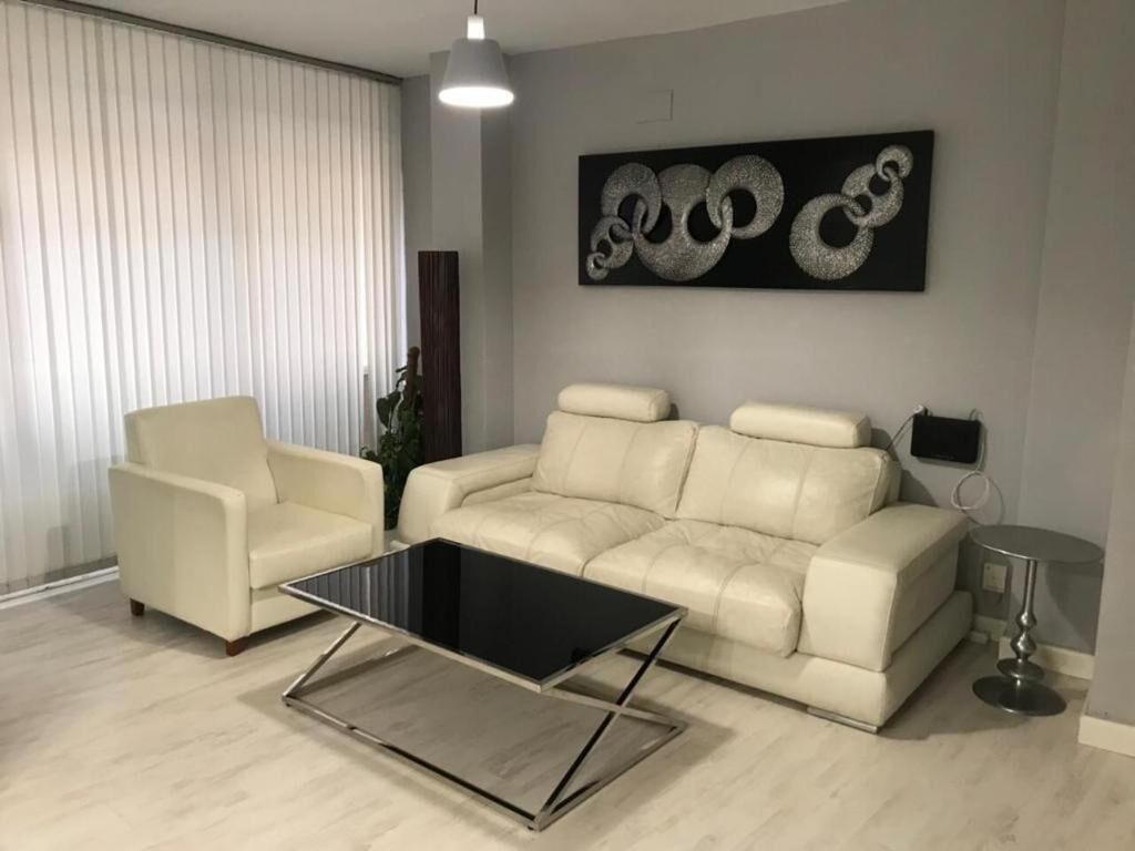 Uma sala de estar moderna com um sofá bege, uma mesa de centro de vidro e uma grande obra de arte abstrata na parede.