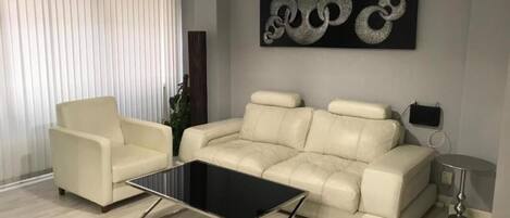 Uma sala de estar moderna com um sofá bege, uma mesa de centro de vidro e uma grande obra de arte abstrata na parede.