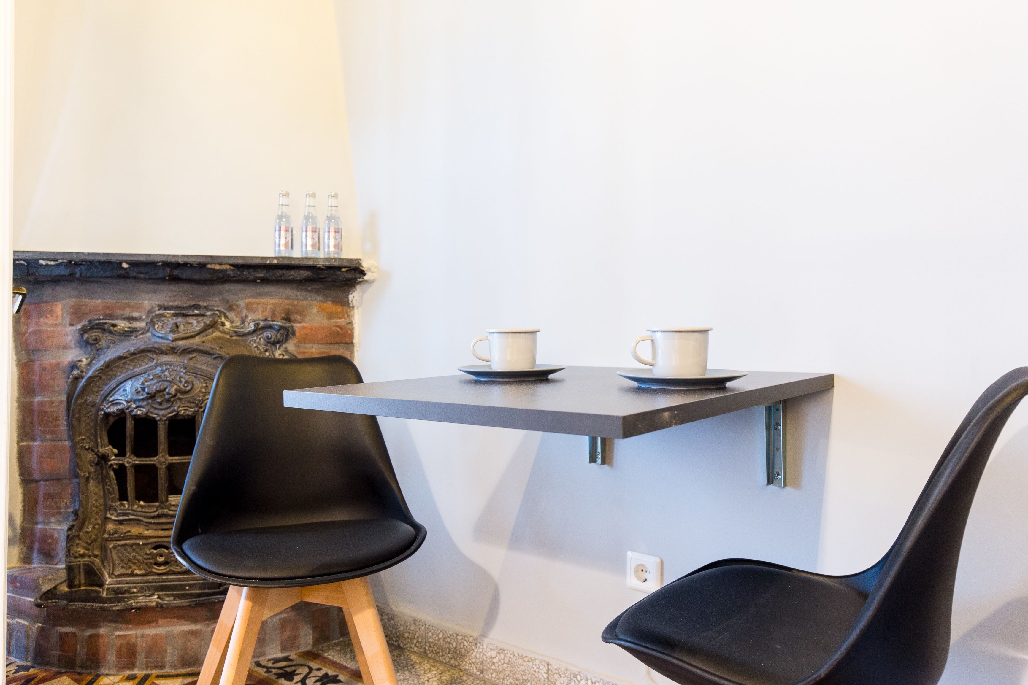 A room with a fireplace, a table with two cups, and two black chairs.