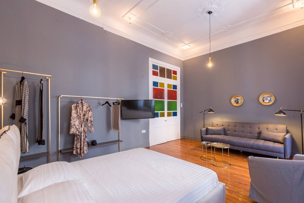 Ein modernes Hotelzimmer mit einem großen Bett, einem grauen Sofa, einem Fernseher und einem Kleiderschrank mit Kleidung.