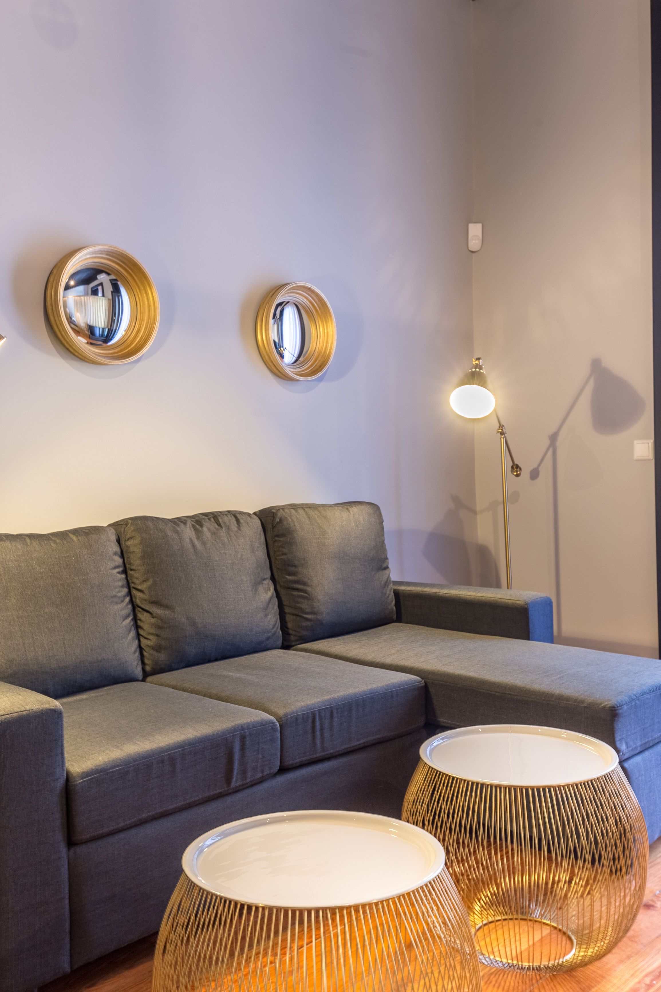 En moderne stue med en grå sofa, to runde spejle på væggen og en gulvlampe.