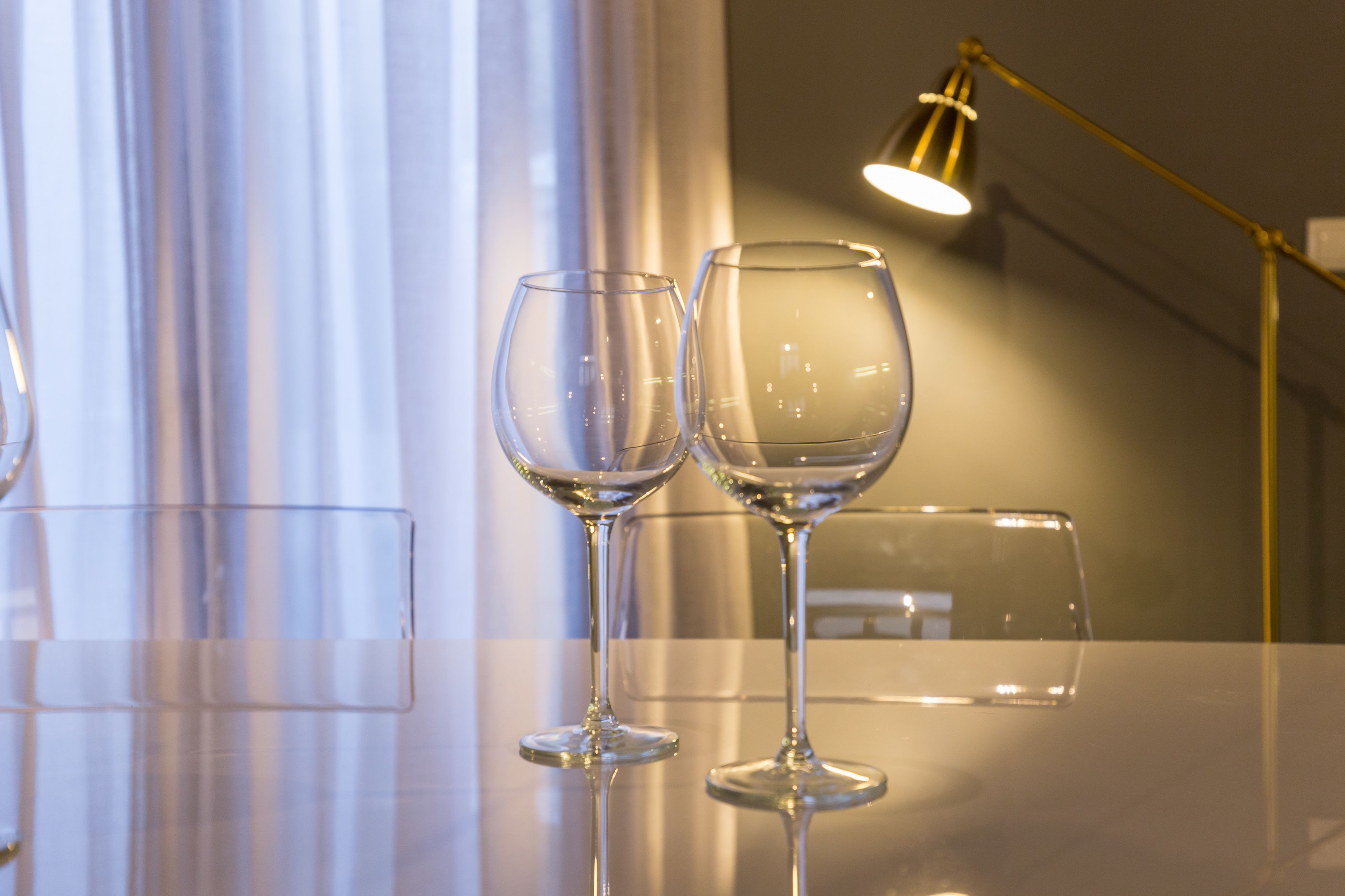 Deux verres à vin vides, posés sur une surface réfléchissante, avec une lampe en arrière-plan.