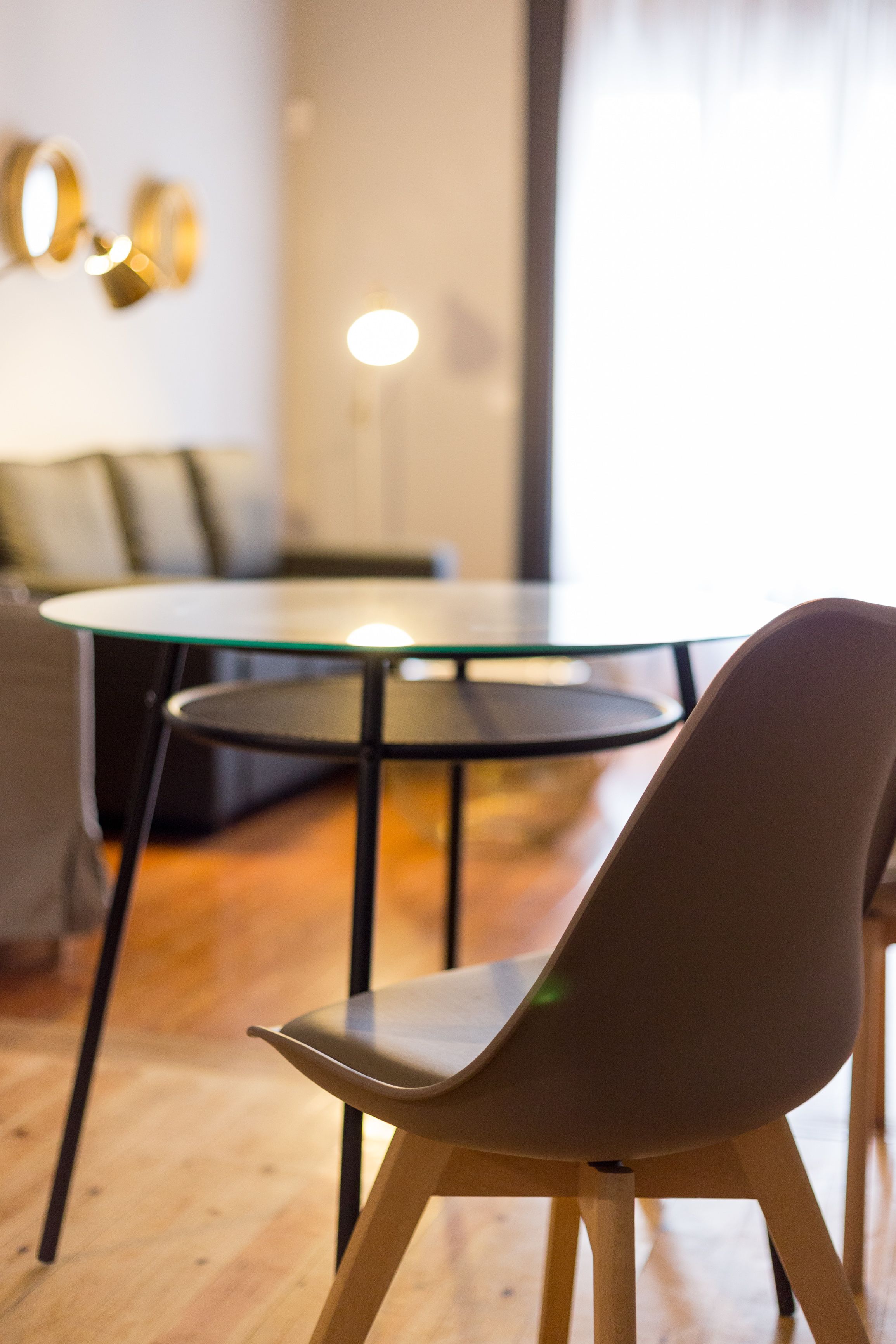Een moderne eetruimte met een glazen tafel en metalen stoelen, een bank en een lamp op de achtergrond.