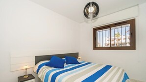 A bedroom with a bed, bedside lamps, a window with bars, and a ceiling light fixture.