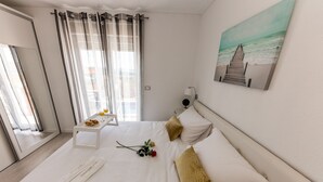 A neatly made bed with white linens, a small bedside table with a plate of food and a glass of drink, and a single red rose. - Villa Hedonist (Seget)